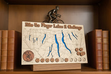 Load image into Gallery viewer, Wooden map of the Bike the Finger Lakes Challenge with engraved lakes and wooden tokens on a bookshelf