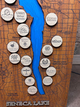 Load image into Gallery viewer, Close-up of laser-engraved maple winery logo tokens on cherry wood Seneca Lake map
