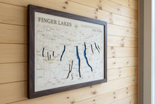 Load image into Gallery viewer, A framed wooden map of Finger Lakes, New York, mounted on a light gray wall. The map features natural wood tones with dark blue laser-etched lake channels and a dark brown wood frame.

